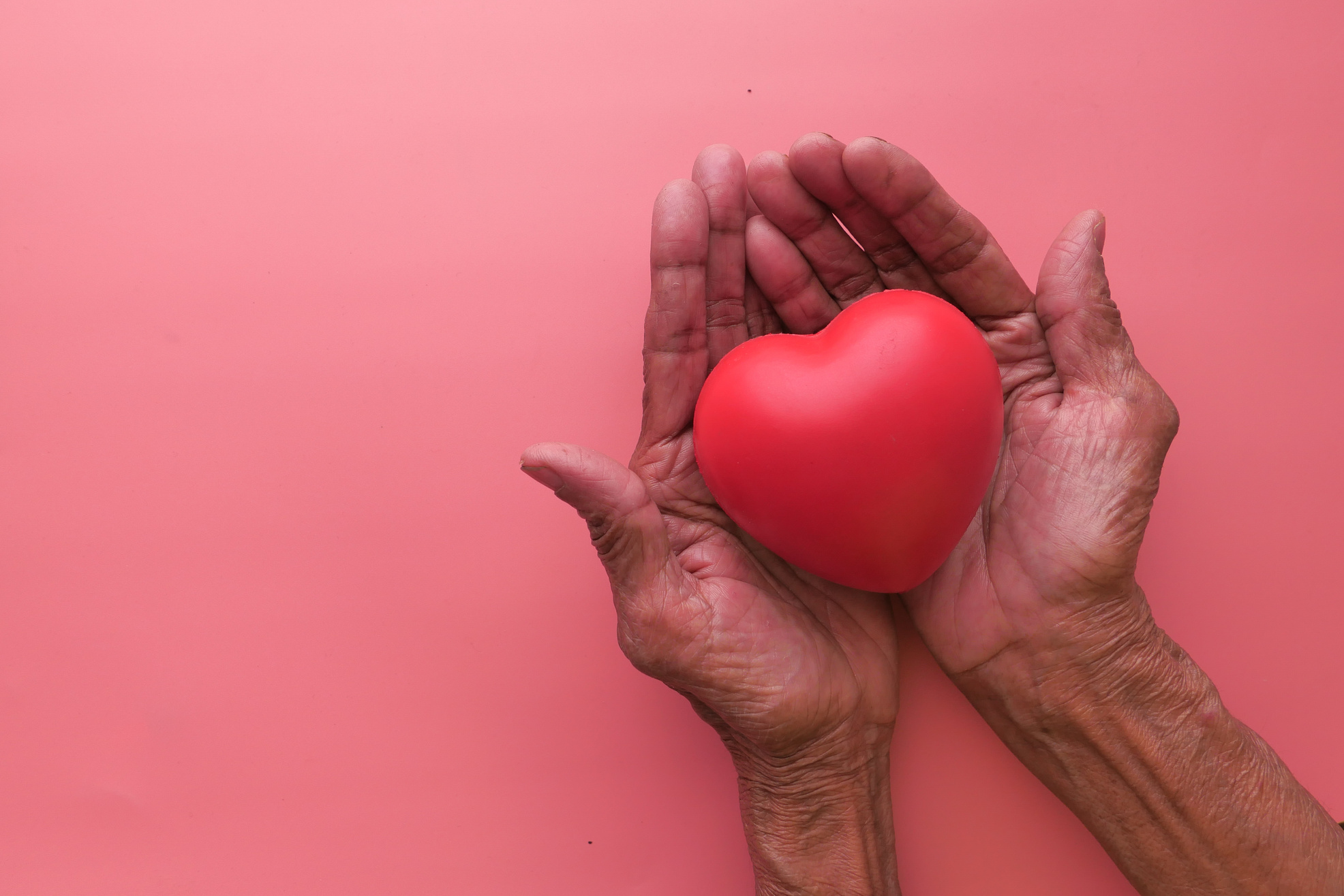 Woman Holding Red Heart in Hands on Wooden Table .